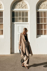 a lady in a black top, a pair of beige pants and a trench coat